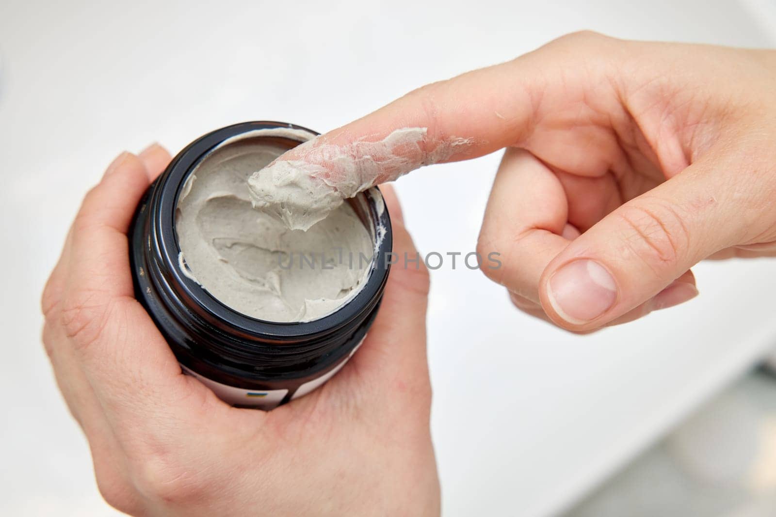 female hand takes a clay face mask from a jar. by erstudio