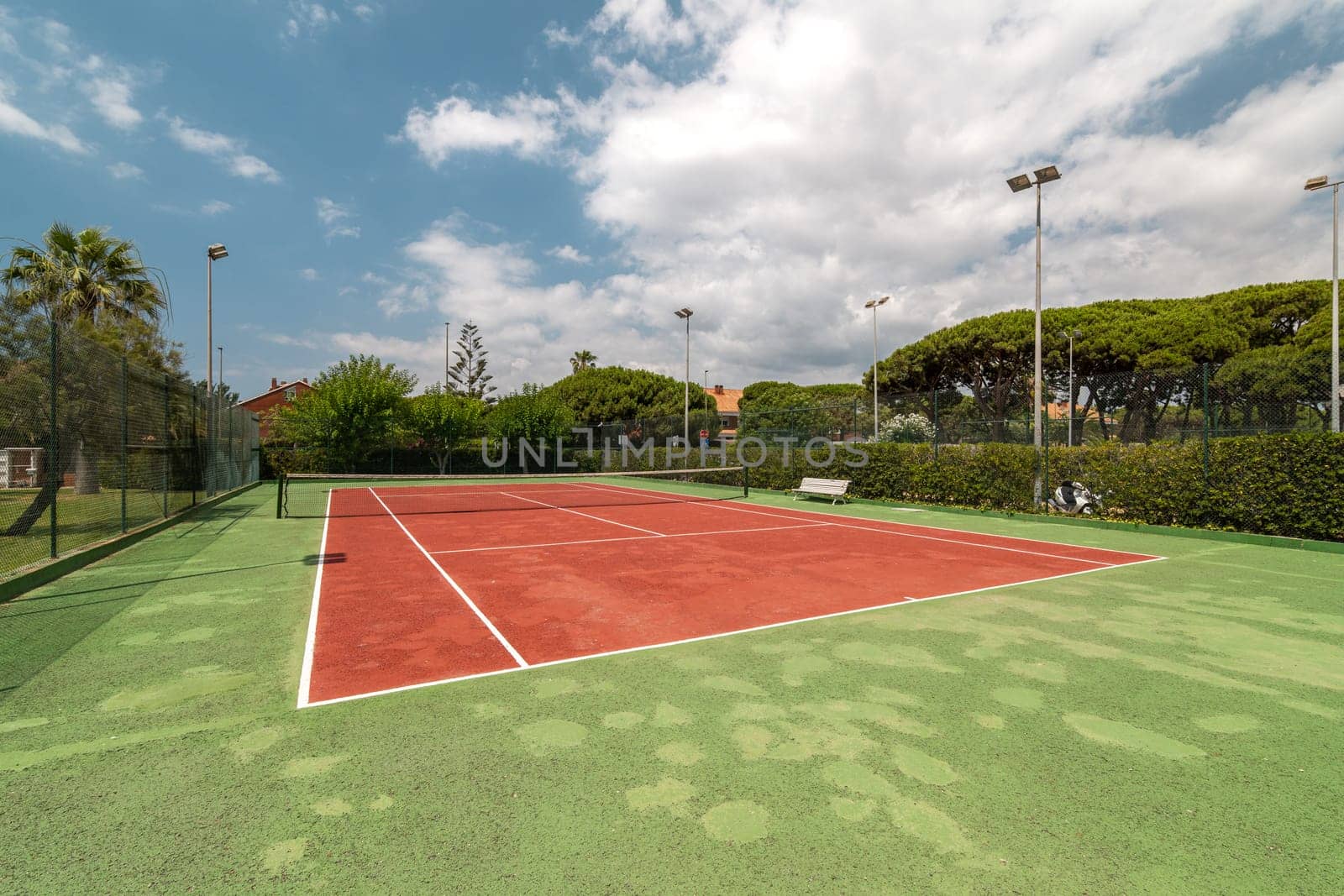 Vibrant outdoor tennis court with a striking red surface, nestled amidst lush greenery.