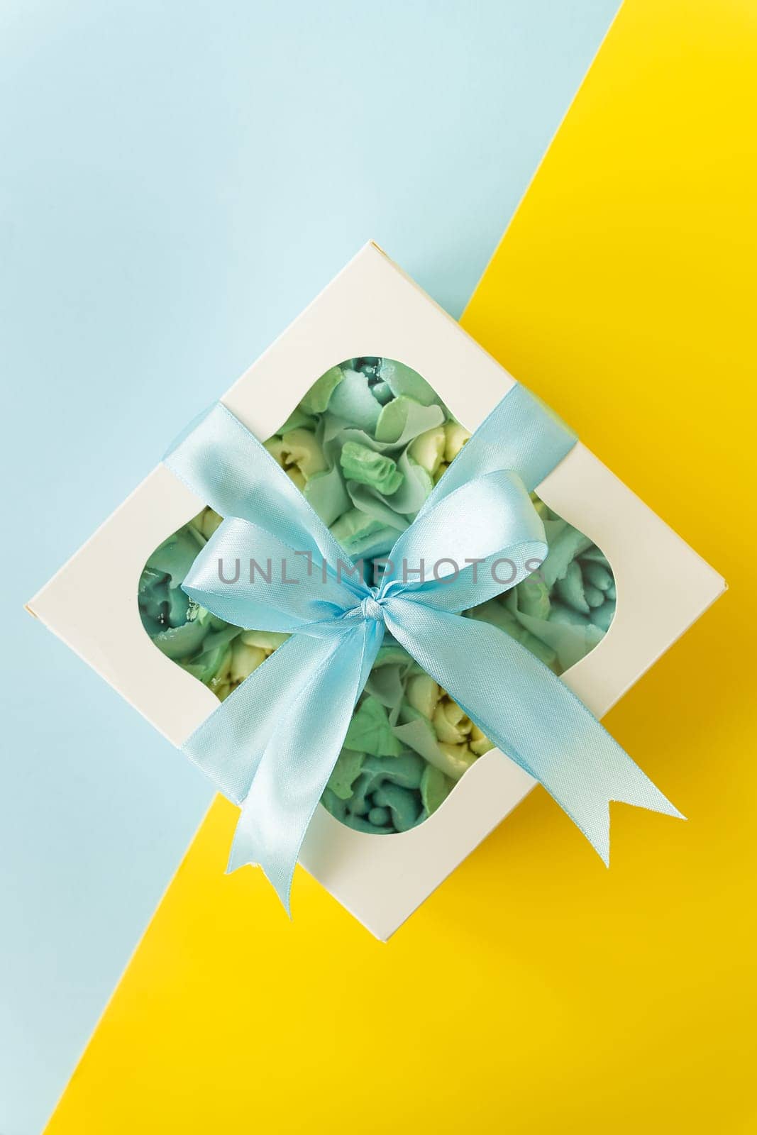 White gift box with pastel blue sweets inside, tied with a blue ribbon on a yellow background. by sfinks