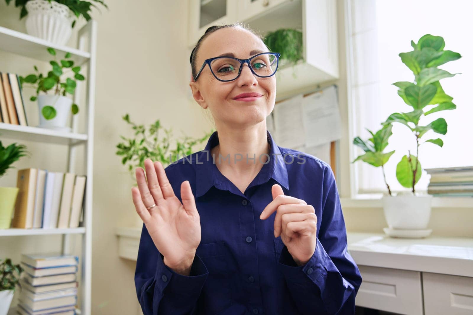 Webcam view of smiling middle-aged woman waving hand. Female blogger vlogger recording video, business lady during video chat conference call, teacher mentor giving online lesson, filming training course