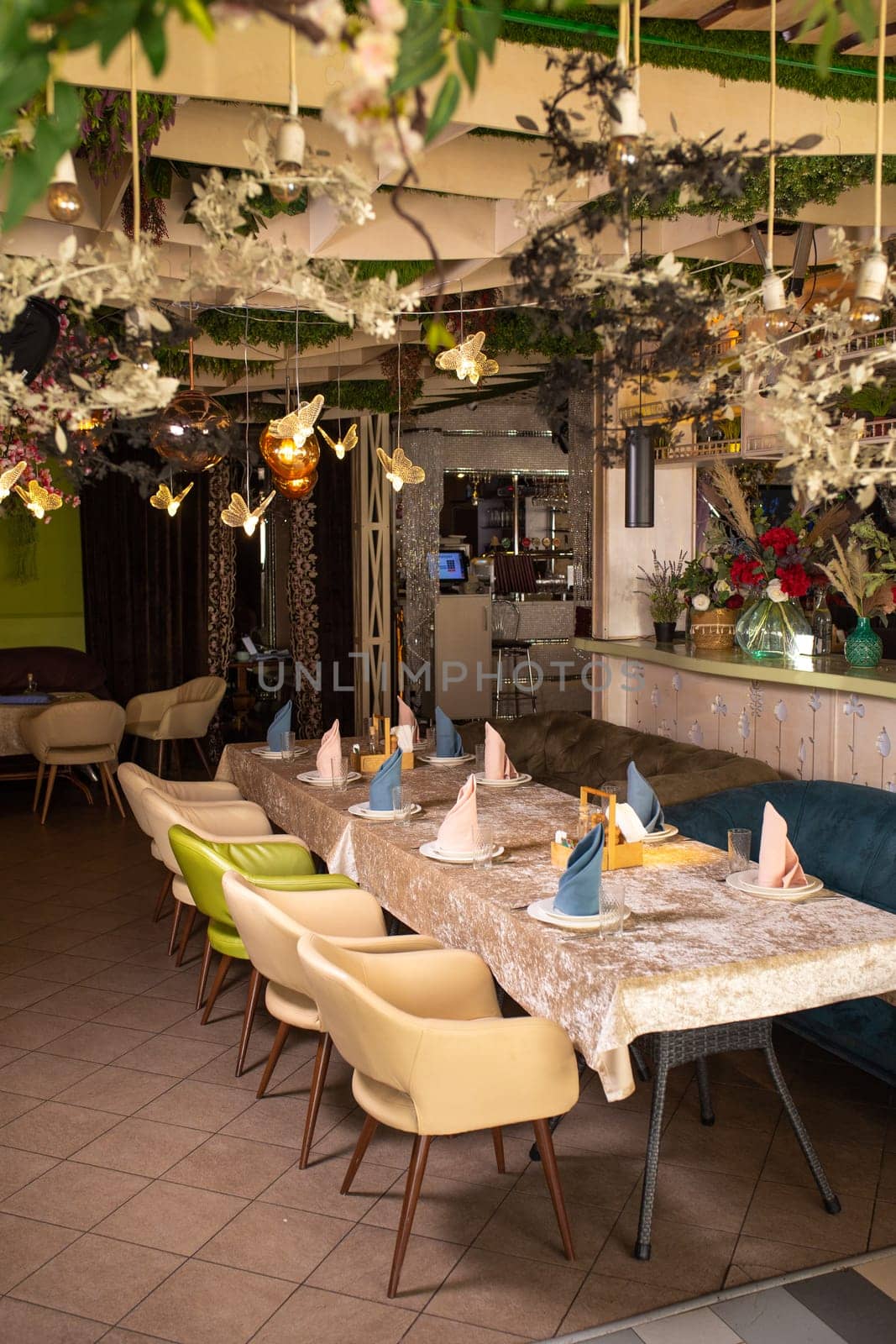 Modern restaurant design with nature touch. Green plants, flowers on walls and ceiling. Long table with glasses, cloth napkins.