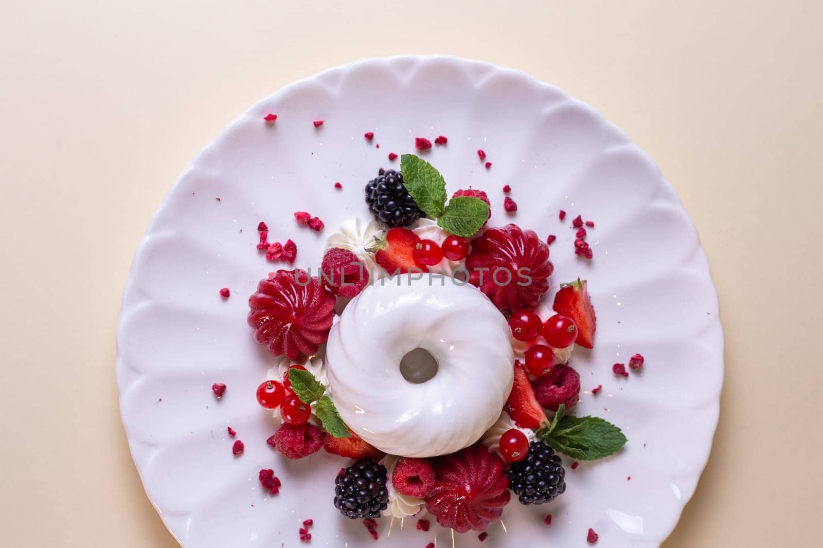 Decadent cake with cream, strawberries, blueberries, raspberries on white plate, isolated on beige background.