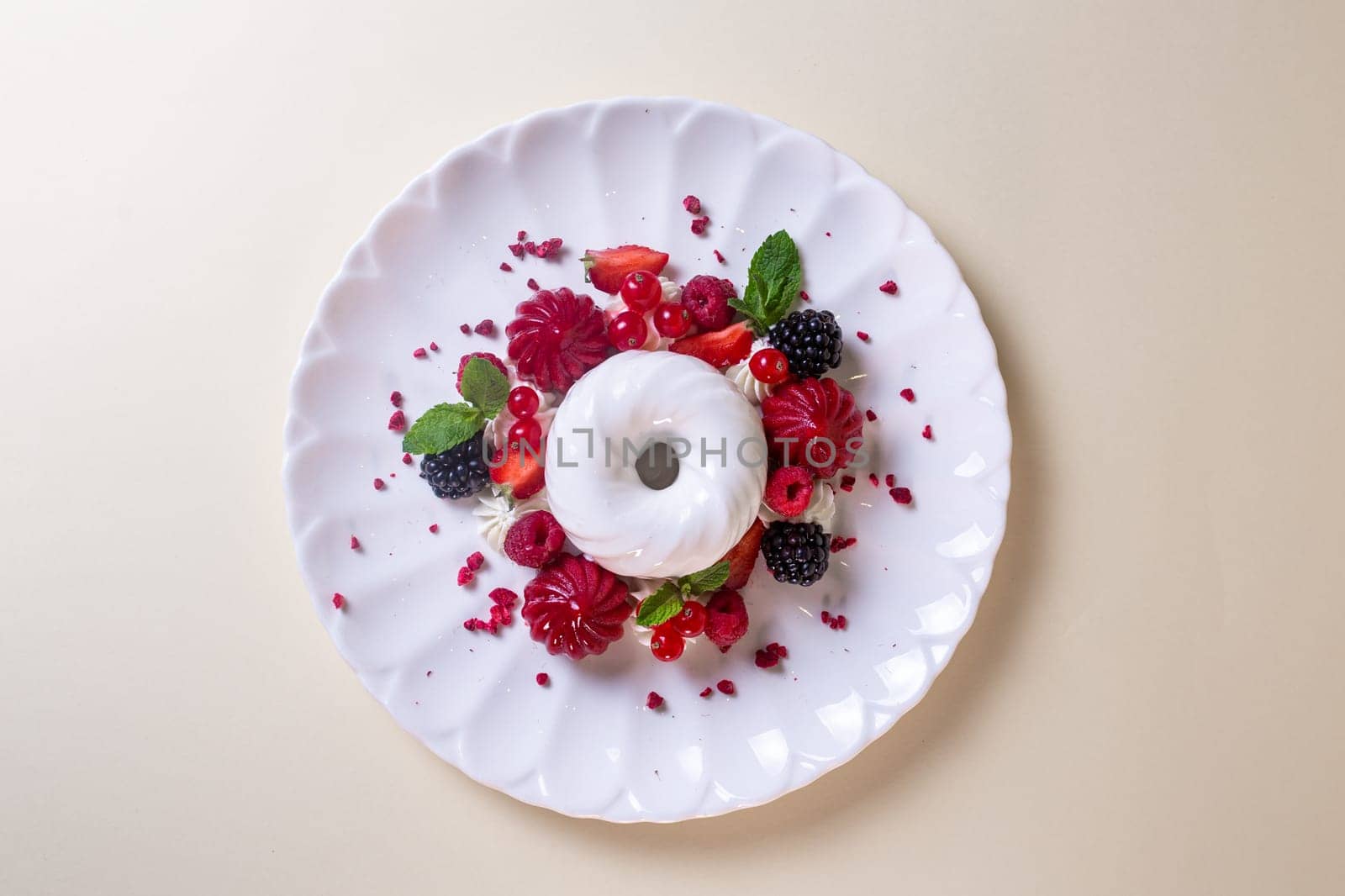 Decadent cake with cream, strawberries, blueberries, raspberries on white plate, isolated on beige background.