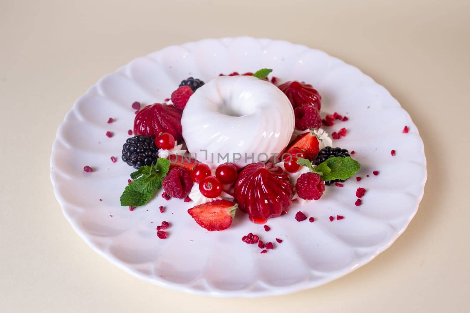 Decadent cake with cream, strawberries, blueberries, raspberries on white plate, isolated on beige background.