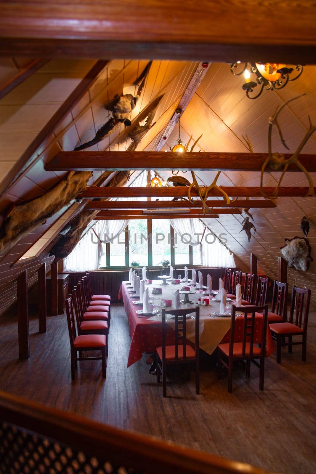 Rustic lodge interior with chandelier, red tableschairs, and mounted animal headsantlers. Ideal background for huntingnature themes.