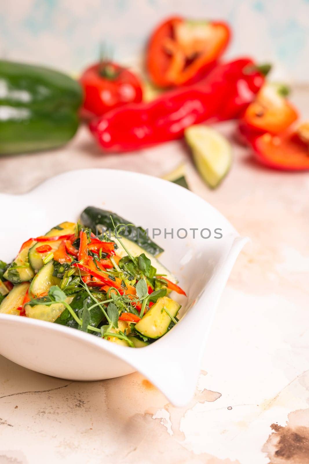 Fresh cucumbers, bell peppers, and herbs on white plate, pink background by Pukhovskiy