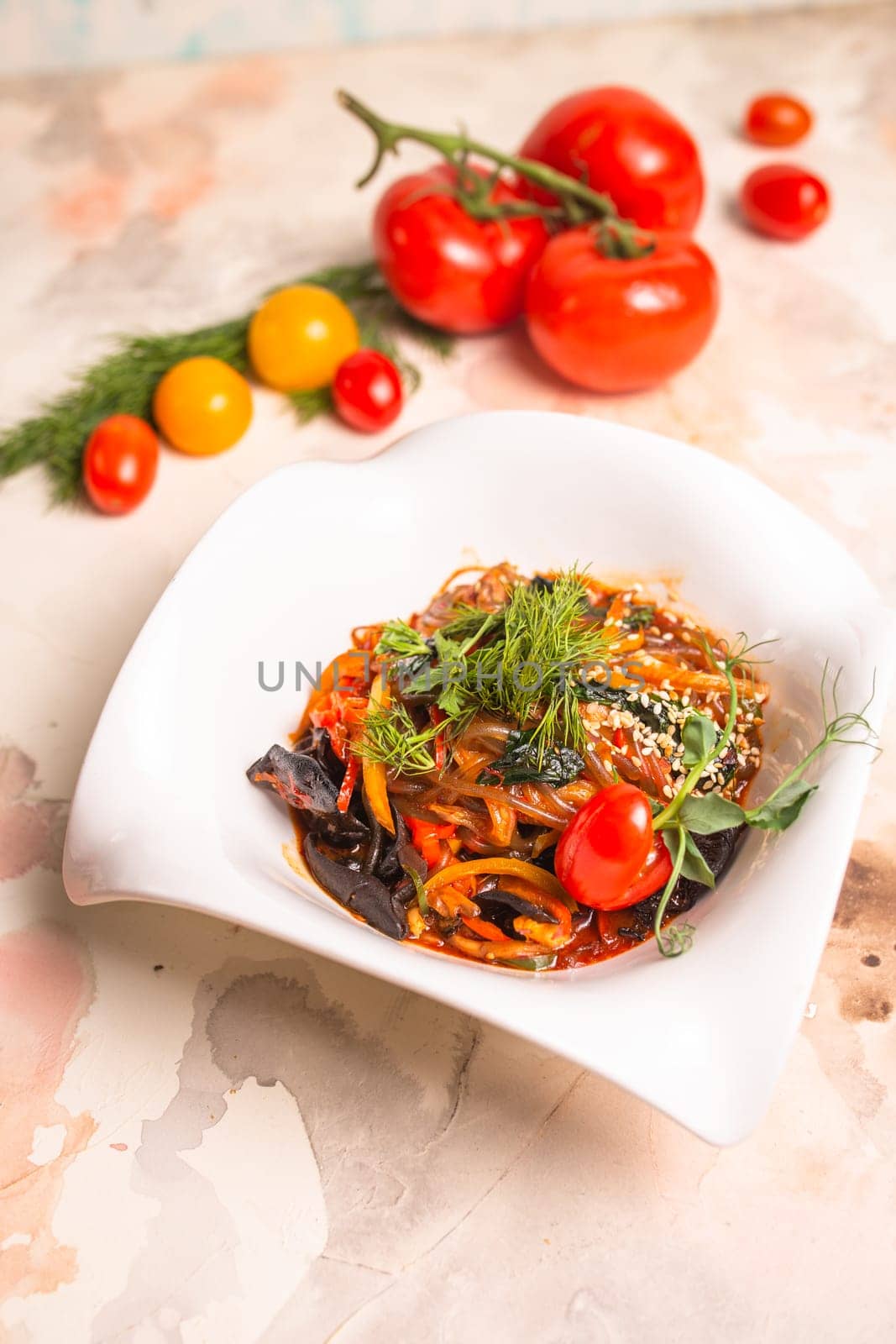 A delicious and healthy meal of Japchae, made with sweet potato noodles, vegetables, and a savory sauce, garnished with tomatoes and dill