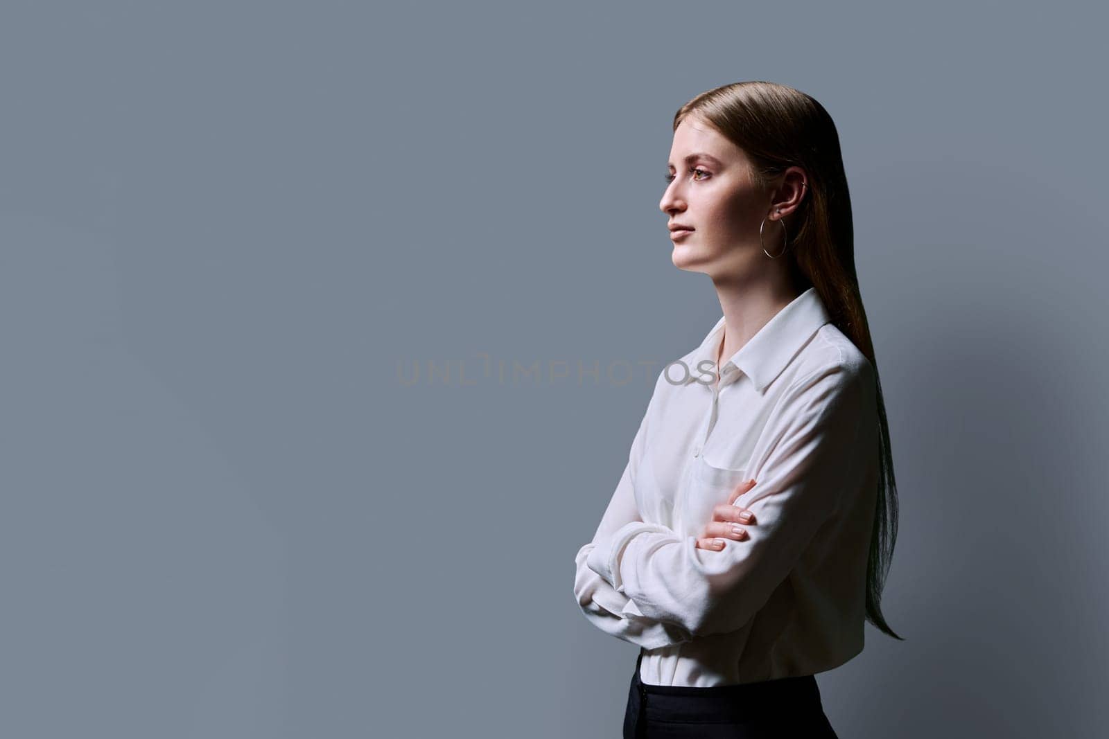 Profile view, confident serious successful young teenage woman with crossed arms, copy space gray studio background, space for advertising image text. Education services people concept