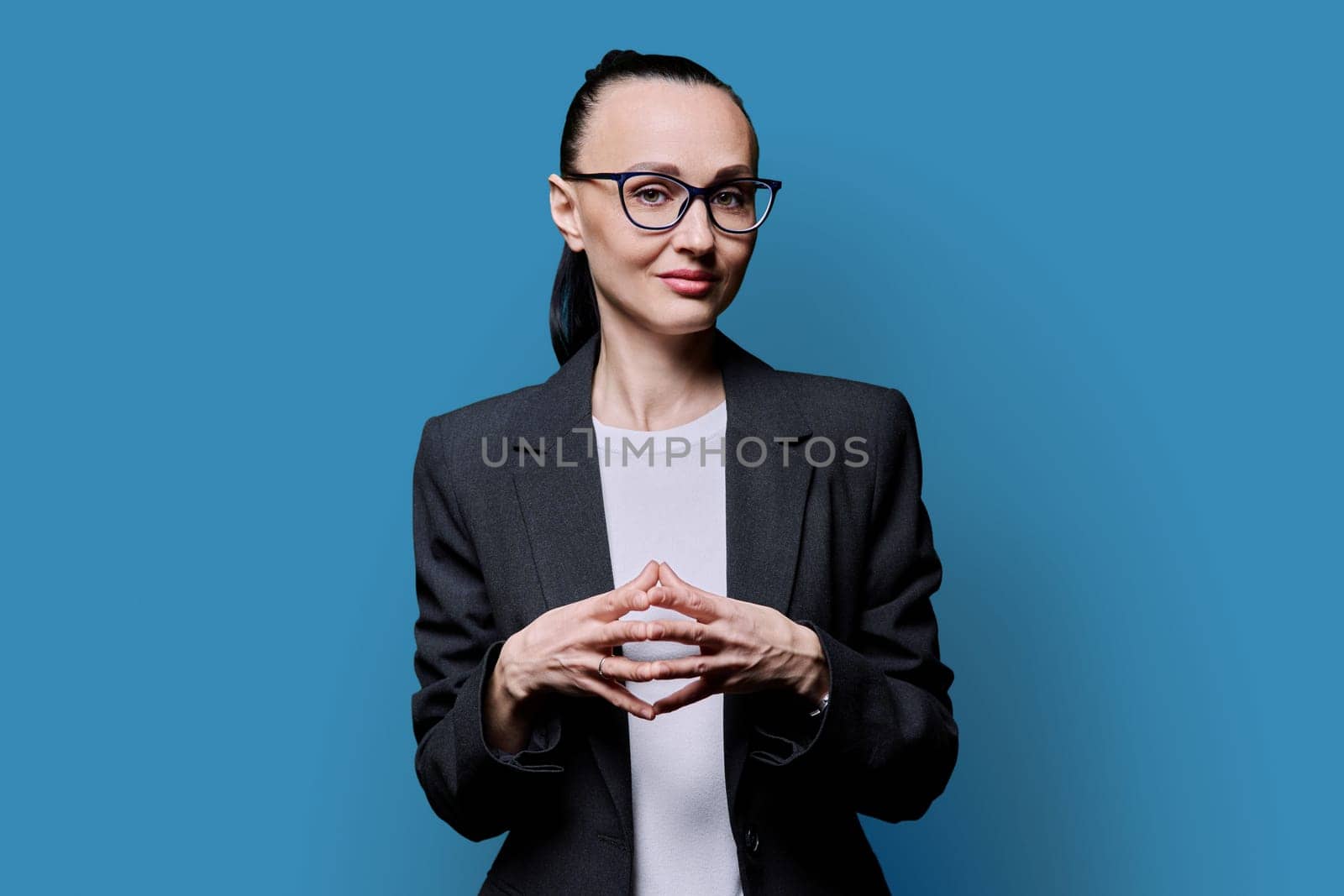 Portrait of thinking serious 30s business woman on blue studio background. Confident female in glasses, suit looking at camera. Business work teaching job career people concept