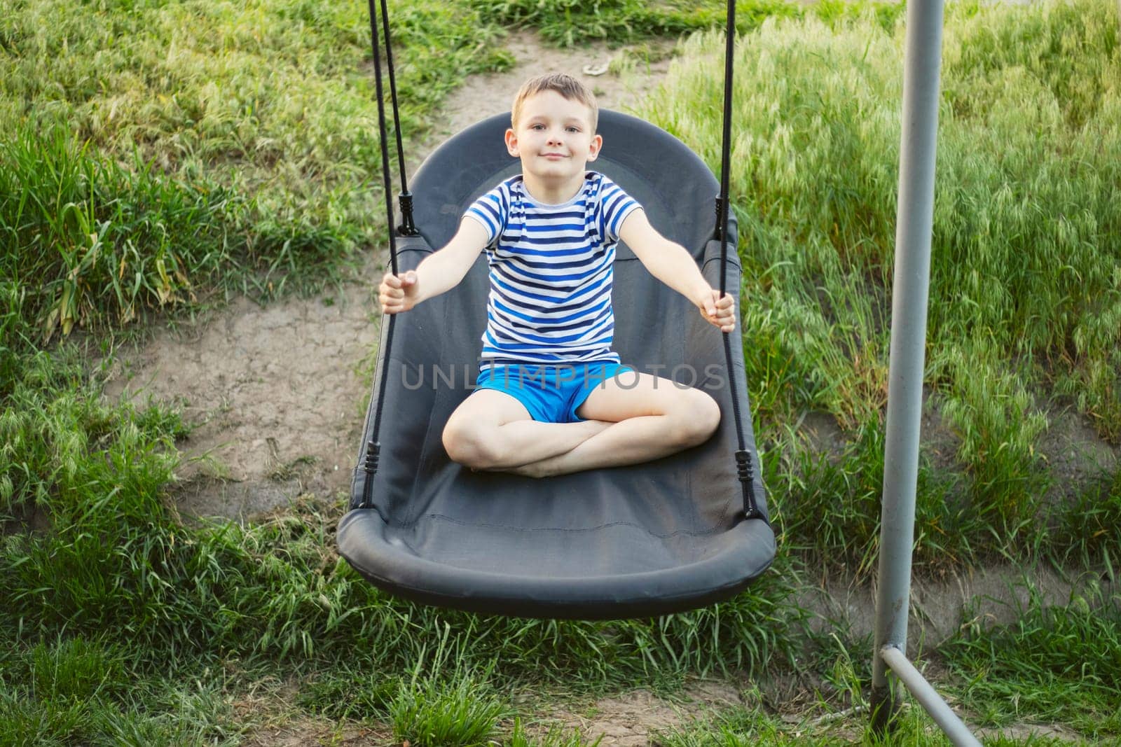 Young boy sitting on swing outdoors in summer. Leisure, childhood concept. Lifestyle portrait, natural, candid design for family, leisure banner.