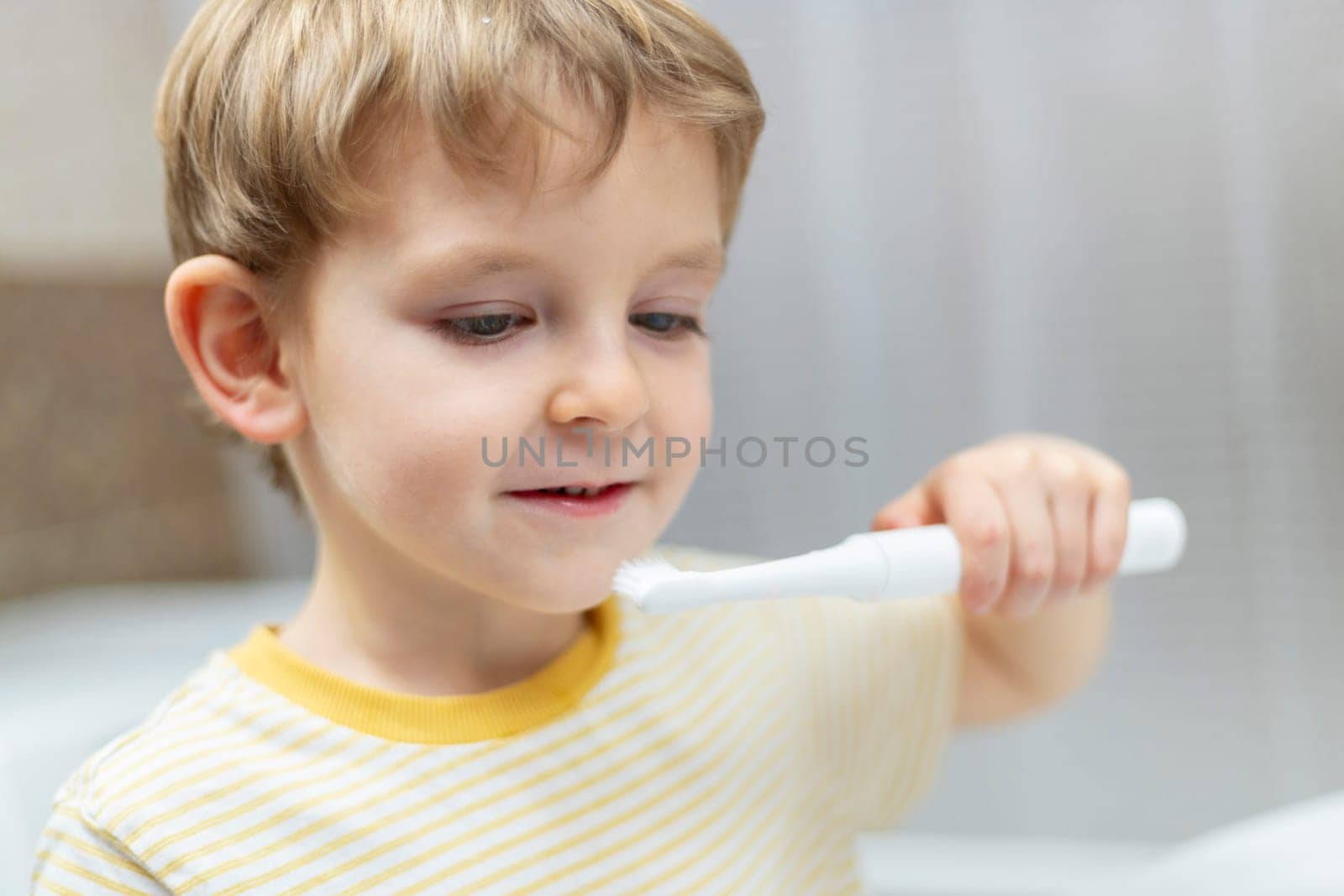 Young boy brushing teeth with electric toothbrush in bathroom. Candid domestic scene.