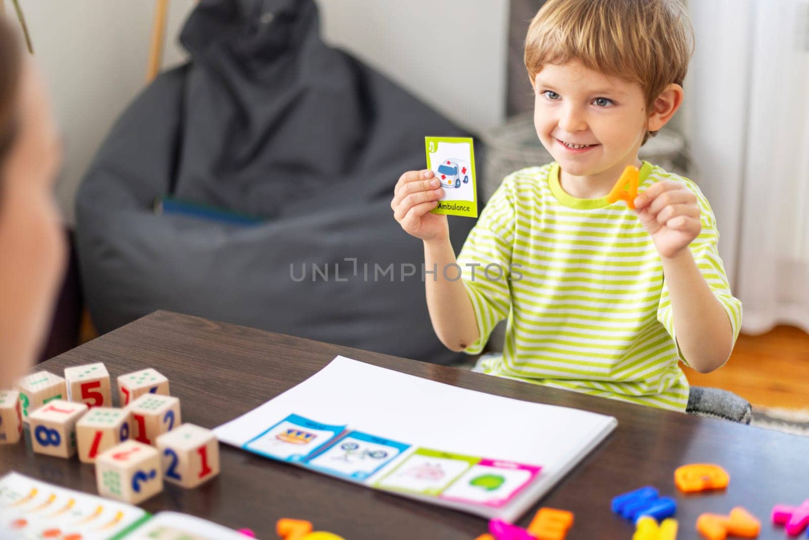 Smiling boy playing learning game with cards and colorful letters. Educational activity concept.