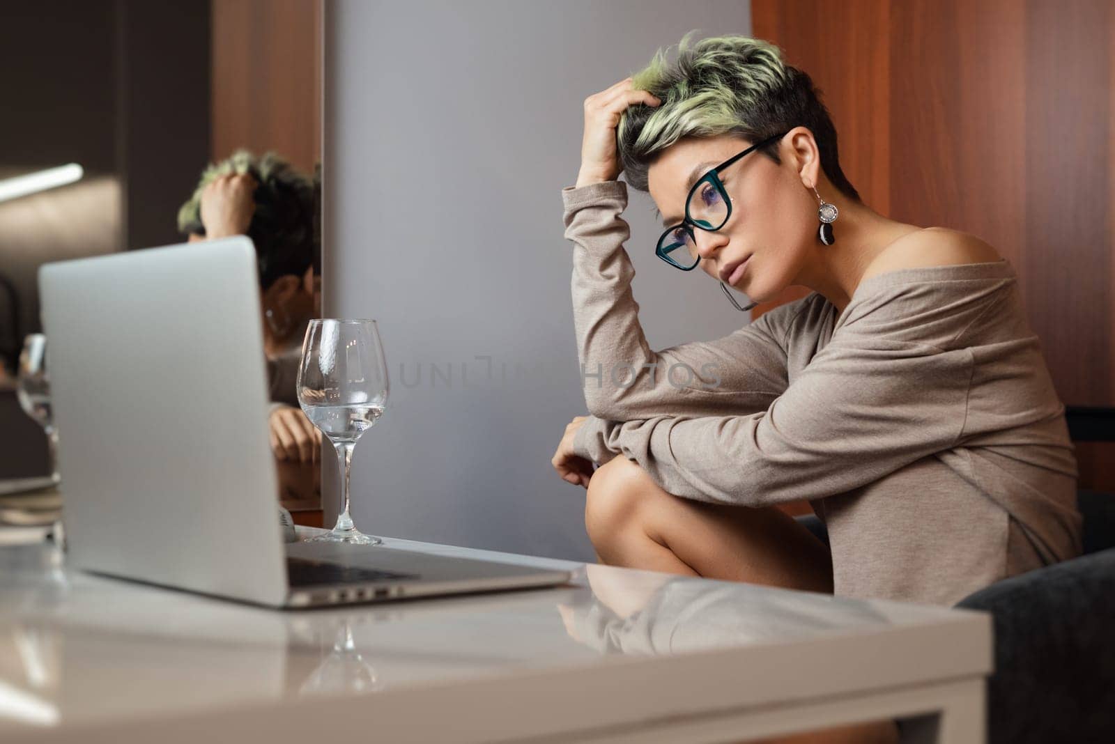 a beautiful girl with short hair and glasses is sitting indoors at a laptop chatting and working online