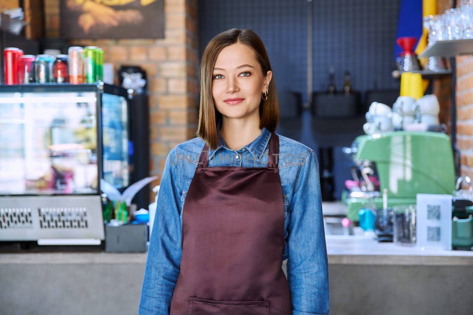 Confident successful young woman service worker in apron looking at camera in restaurant cafeteria coffee shop pastry shop. Small business, staff, occupation, entrepreneur owner, work concept