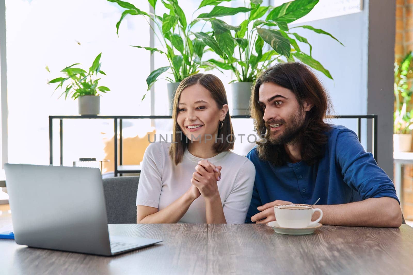 Happy smiling surprised young couple looking at laptop together while sitting in cafe, cafeteria. Leisure time for two, lifestyle, togetherness, relationship, communication, work study remotely