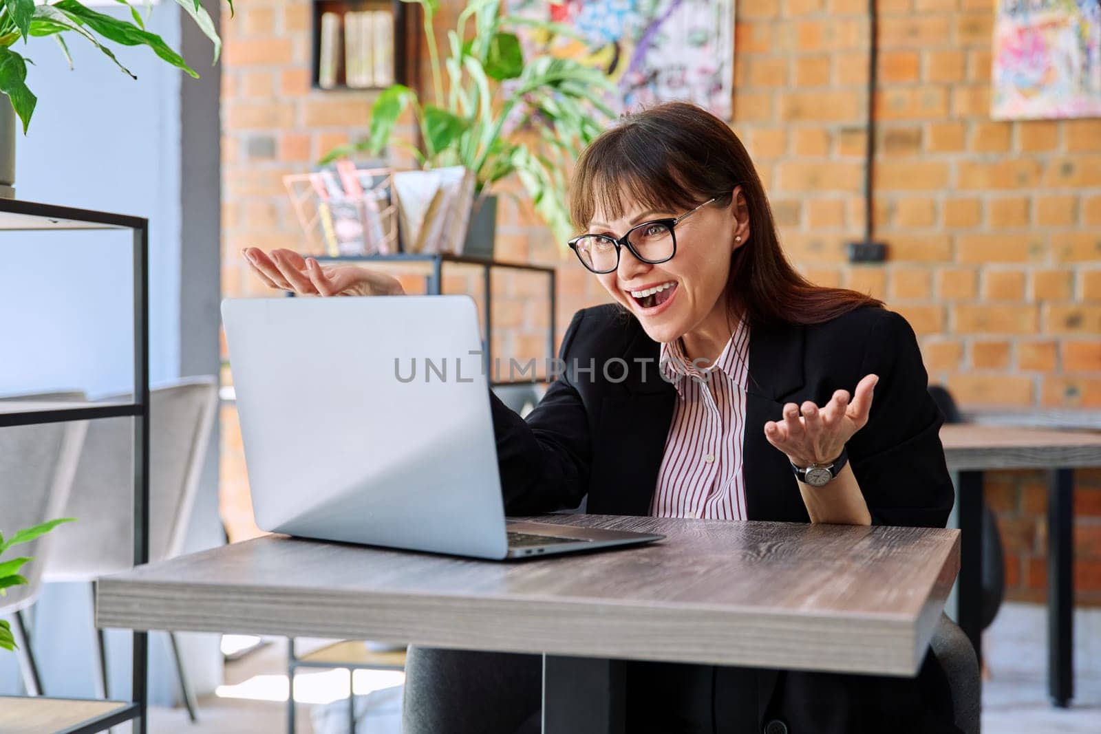 Cheerful talking middle-aged woman having video call chat conference using laptop computer, sitting in coworking cafe. Business, online internet technology, success leadership management empowerment