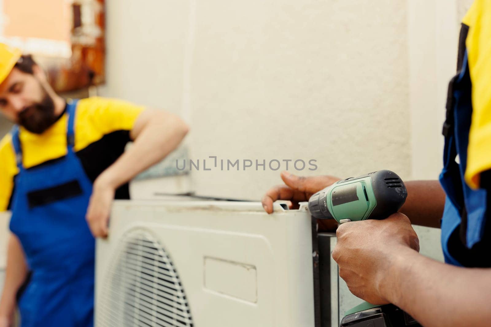 Expert repairmen fixing outdoor air conditioner for home owner. Competent mechanic coworkers commissioned to do maintenance on condenser, ensuring it operates at maximum efficiency