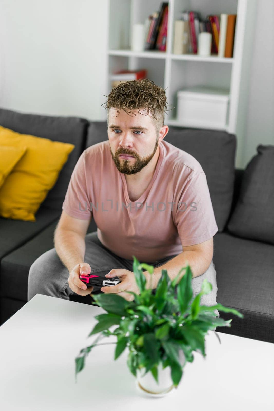 Young man spending time at home, sitting on a couch in apartment and playing arcade car video games on console. Male using controller to play street racing drift simulator. by Satura86