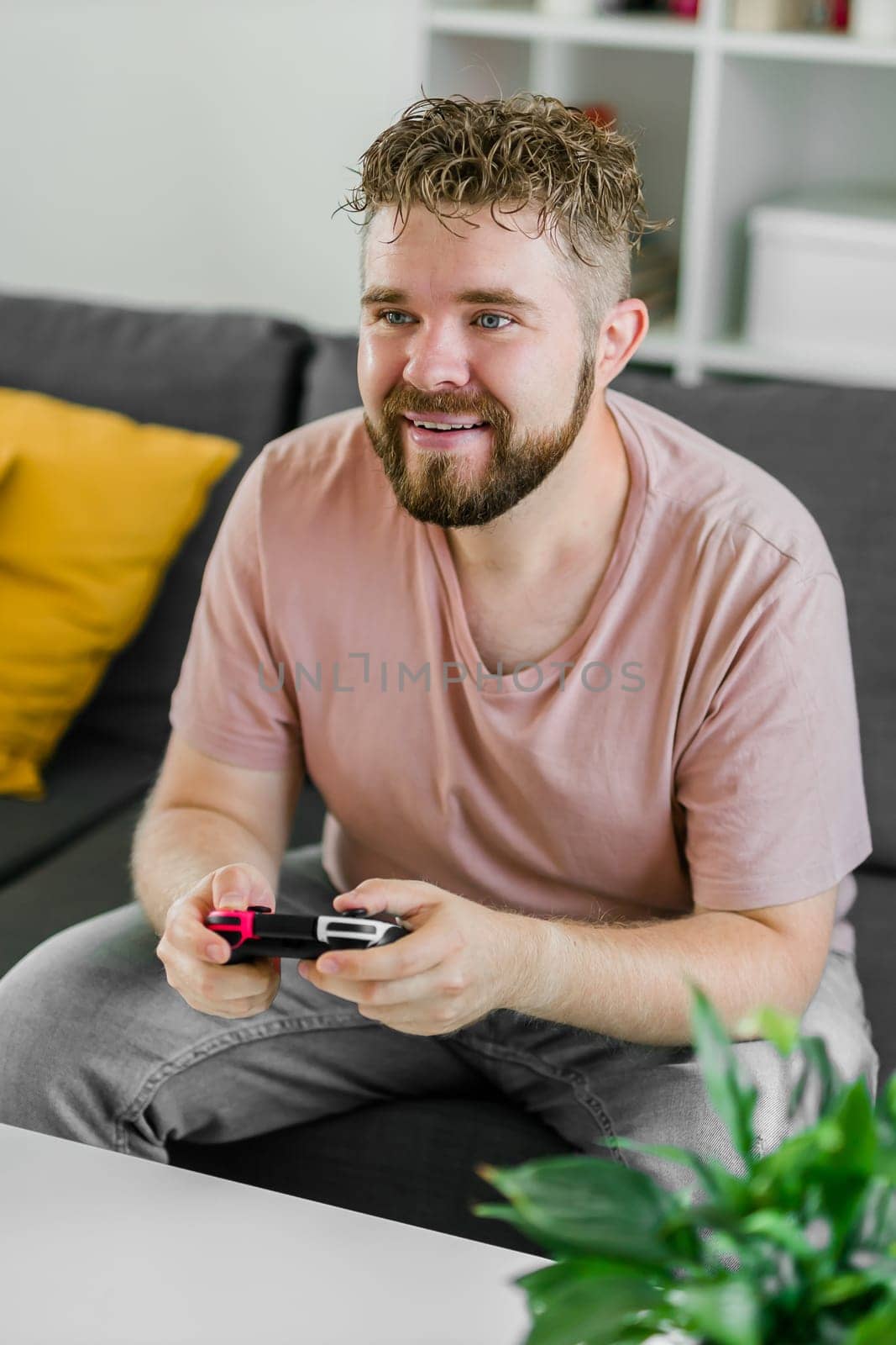 Cheerful young man seated on a sofa playing video games at home. Gaming addiction and entertainment.