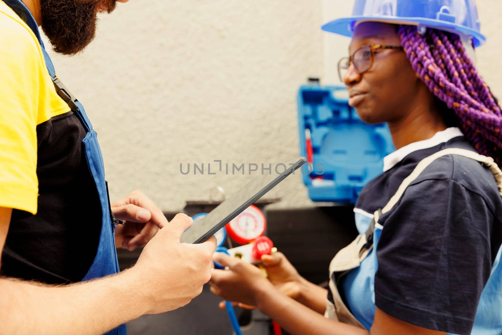 Seasoned mechanic coworkers refilling freon and repairing leaks in outdoor hvac system. Knowleadgeable engineers diagnosing air conditioner to prevent refrigerant loss and ensure optimal performance