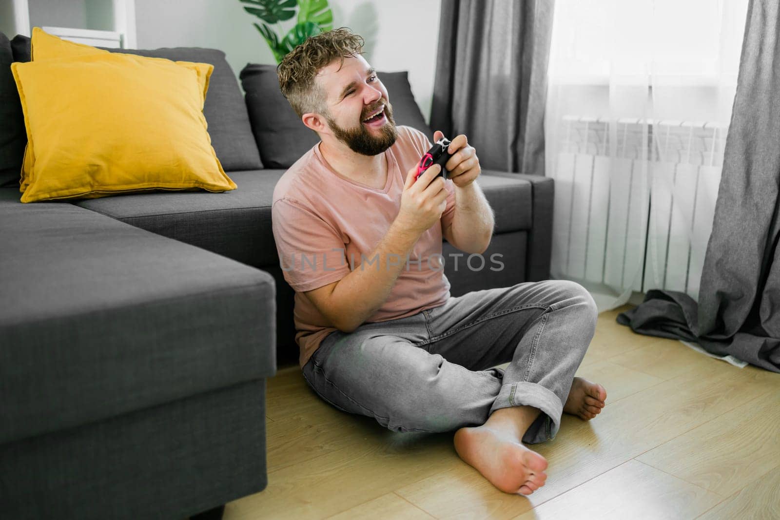 Young man spending time at home, sitting on a floor in apartment and playing arcade car video games on console. Male using controller to play street racing drift simulator. by Satura86