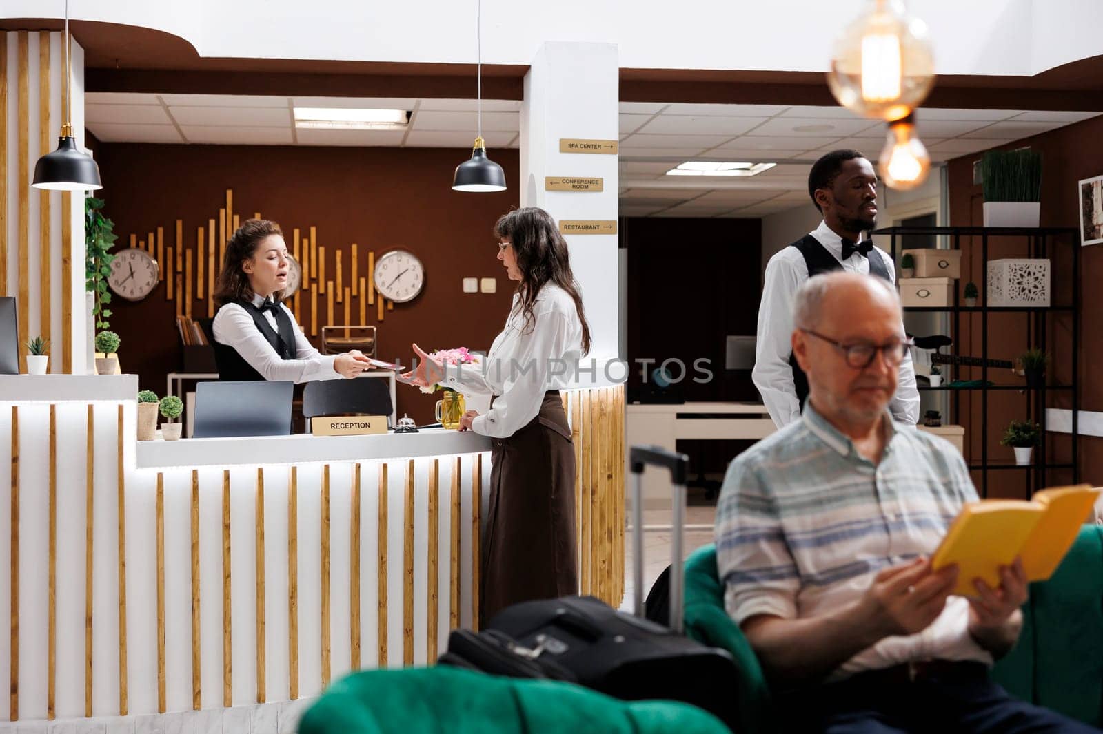 Senior caucasian woman standing at hotel lobby counter and checks in with passport. Female concierge at registration desk returning personal document of elderly lady traveler after verfiying identity.