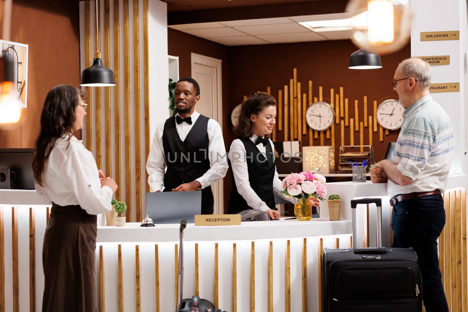 Employees assisting elderly male and female travelers at registration counter of hotel reception. Multiethnic receptionists welcoming senior visitors, providing helpful information for check-in.