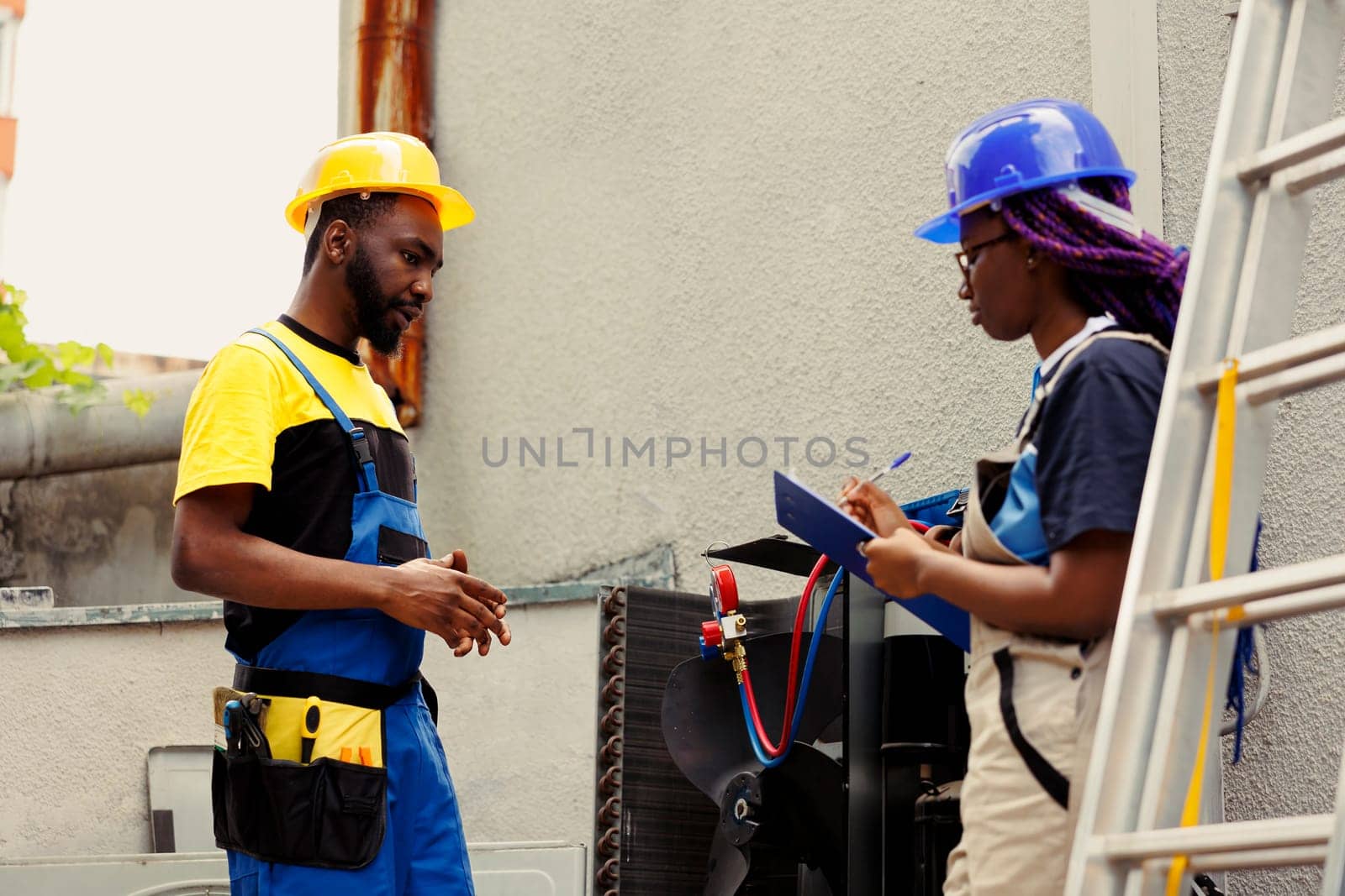 Seasoned mechanics repairing heating and ventilation of air conditioning system. Adept repairmen commissioned for external hvac system yearly maintenance, writing report on clipboard