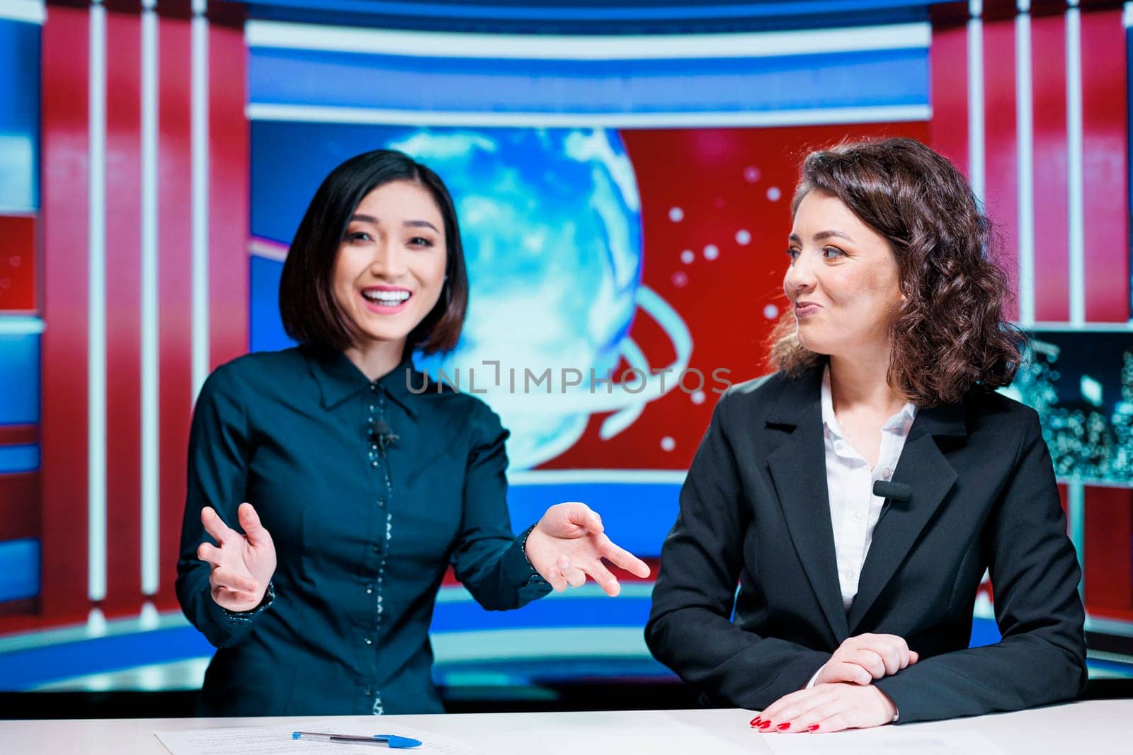 Morning show hosts debate events, presenting latest news on international television network in newsroom. Tewo colleagues working on entertainment segment newscast doing reportage.