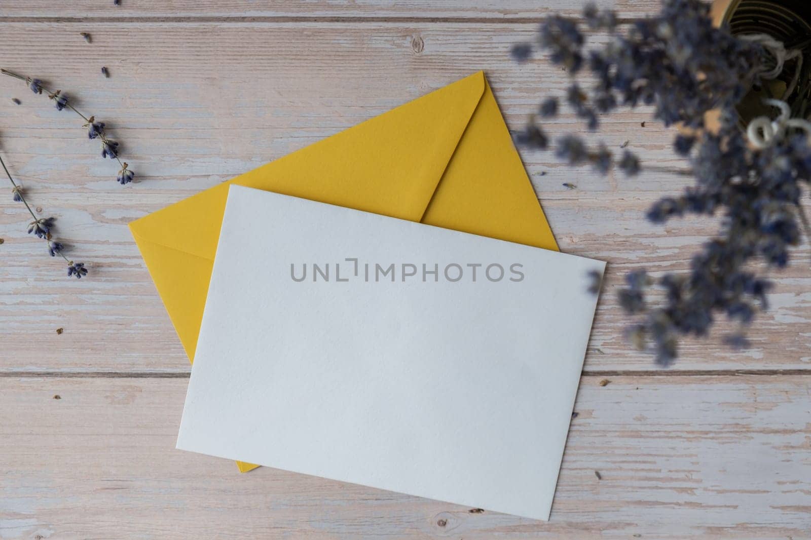 Flat lay composition of white paper greeting card on envelope with dry lavender flowers. Copy space template mock up. Top view. Concept of Wedding invitation postcard. Business advertisement brand blank