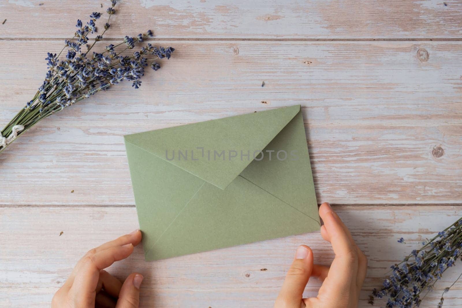 Flat lay composition of female hands holding green envelope with dry lavender flowers. Copy space template mock up. Top view. Concept of Wedding invitation postcard. Business advertisement by anna_stasiia