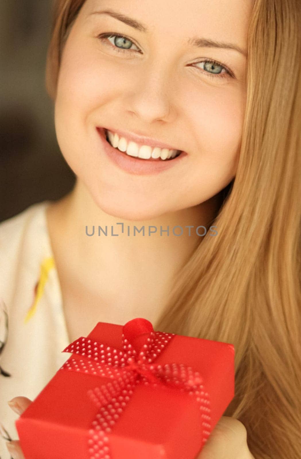 Happy smiling woman holding a red gift box, face portrait with natural make-up and holiday lifestyle at home by Anneleven
