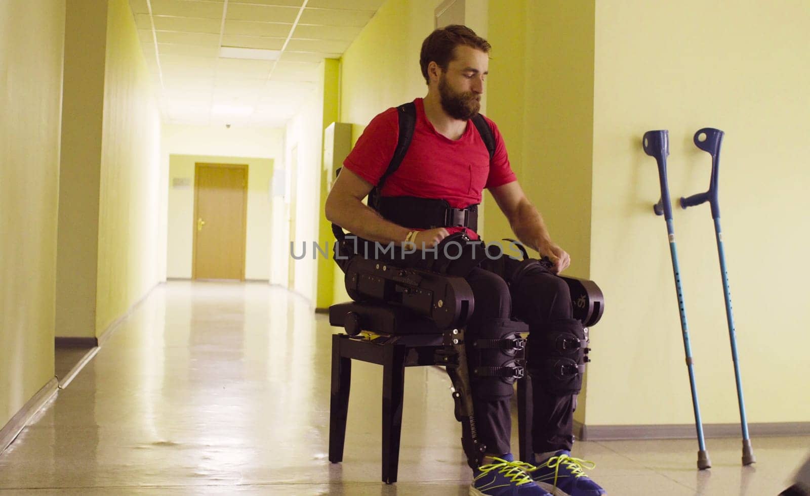 Disable man in the robotic exoskeleton sitting on the bench and taking off exoskeleton