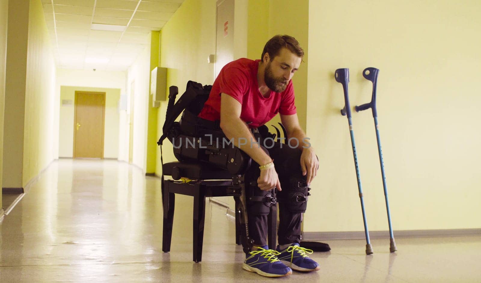 Disable man in the robotic exoskeleton sitting on the bench and taking off exoskeleton