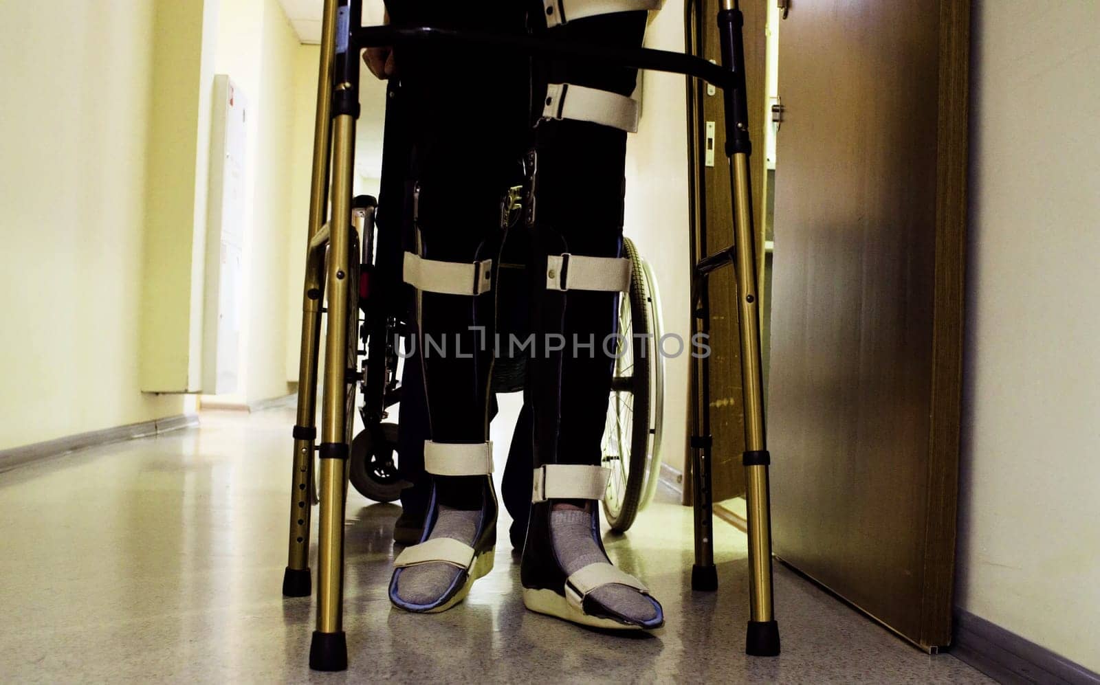 Legs of young disabled man in orthosis walking holding a walking frame through the corridor of the rehabilitation clinic.