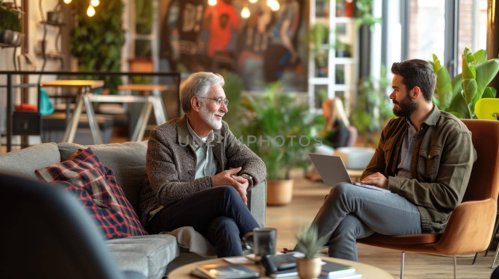 Two men, sitting at a table, are sharing a fun conversation while sporting beards and eyewear. AIG41