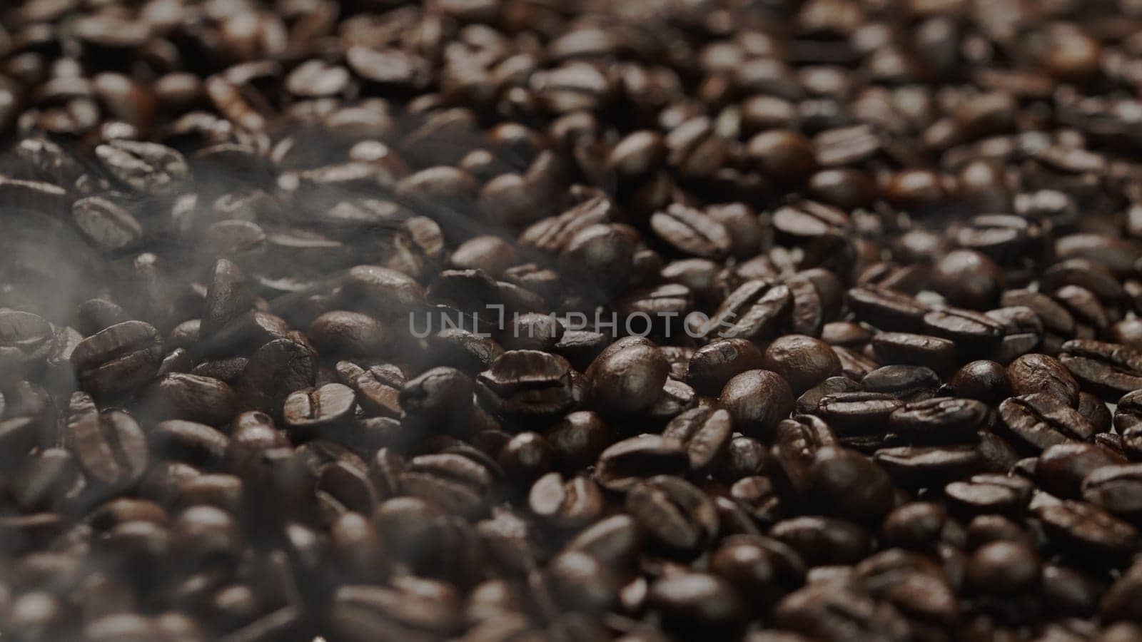 Close up of fresh brown coffee bean with roasted smoke from pile of coffee beans. Macrography of hot coffee seed with fragrant and scented hot smoke come from pile of bean. Top down view. Comestible.