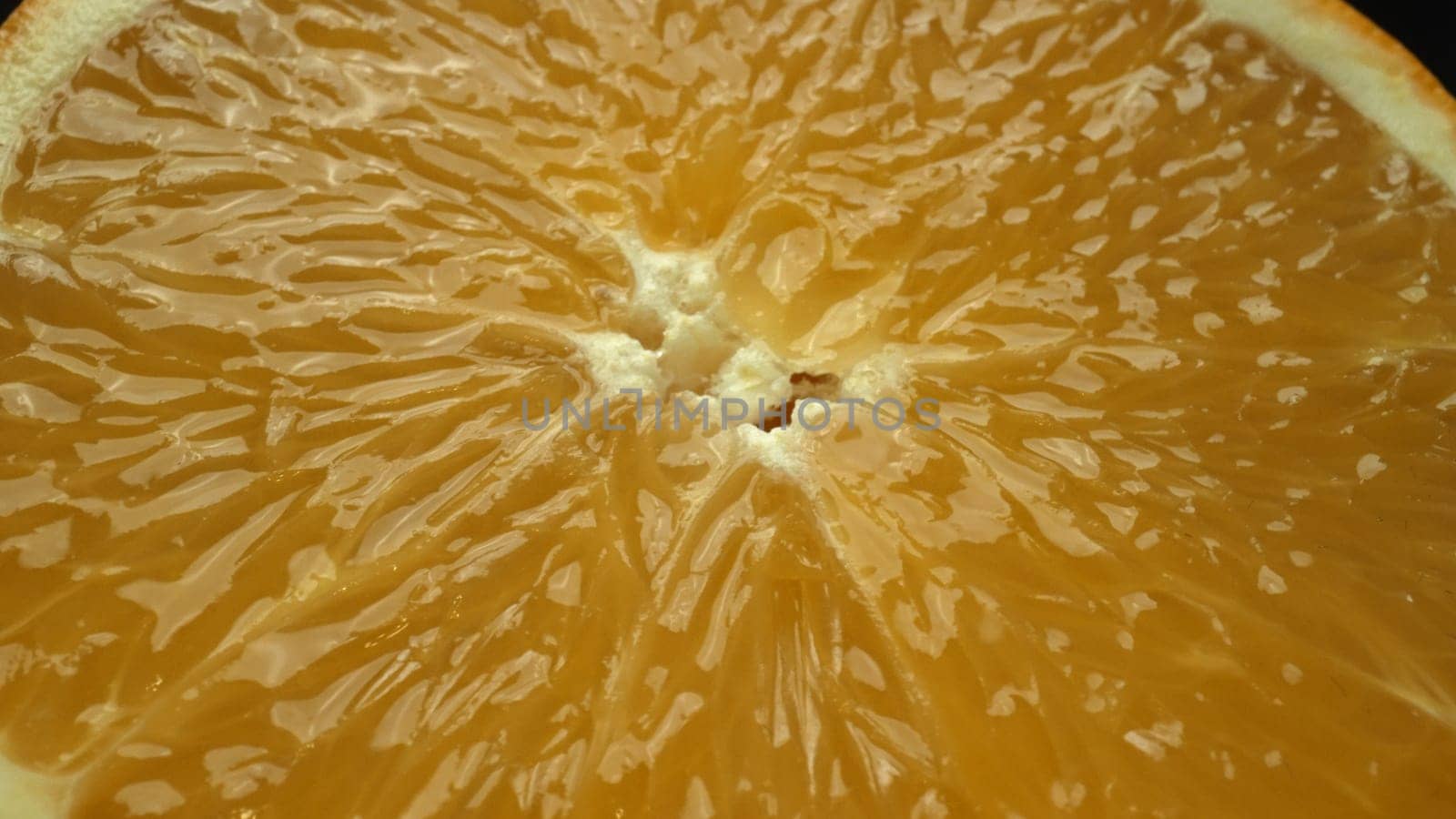 A macrography capture of an orange slice, placed against a sleek, isolated black backdrop, unfolds as a visual masterpiece of citrus allure. A slice of orange with black background. Comestible.