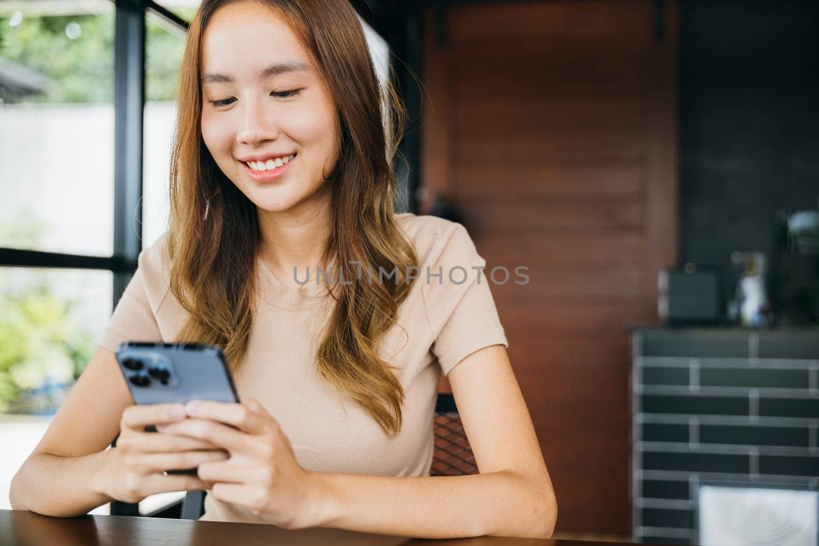 Beautiful Asian female hands holding and typing to communicate with others through on mobile phone, young woman using smartphone for shopping online at cafe coffee shop near windows in morning