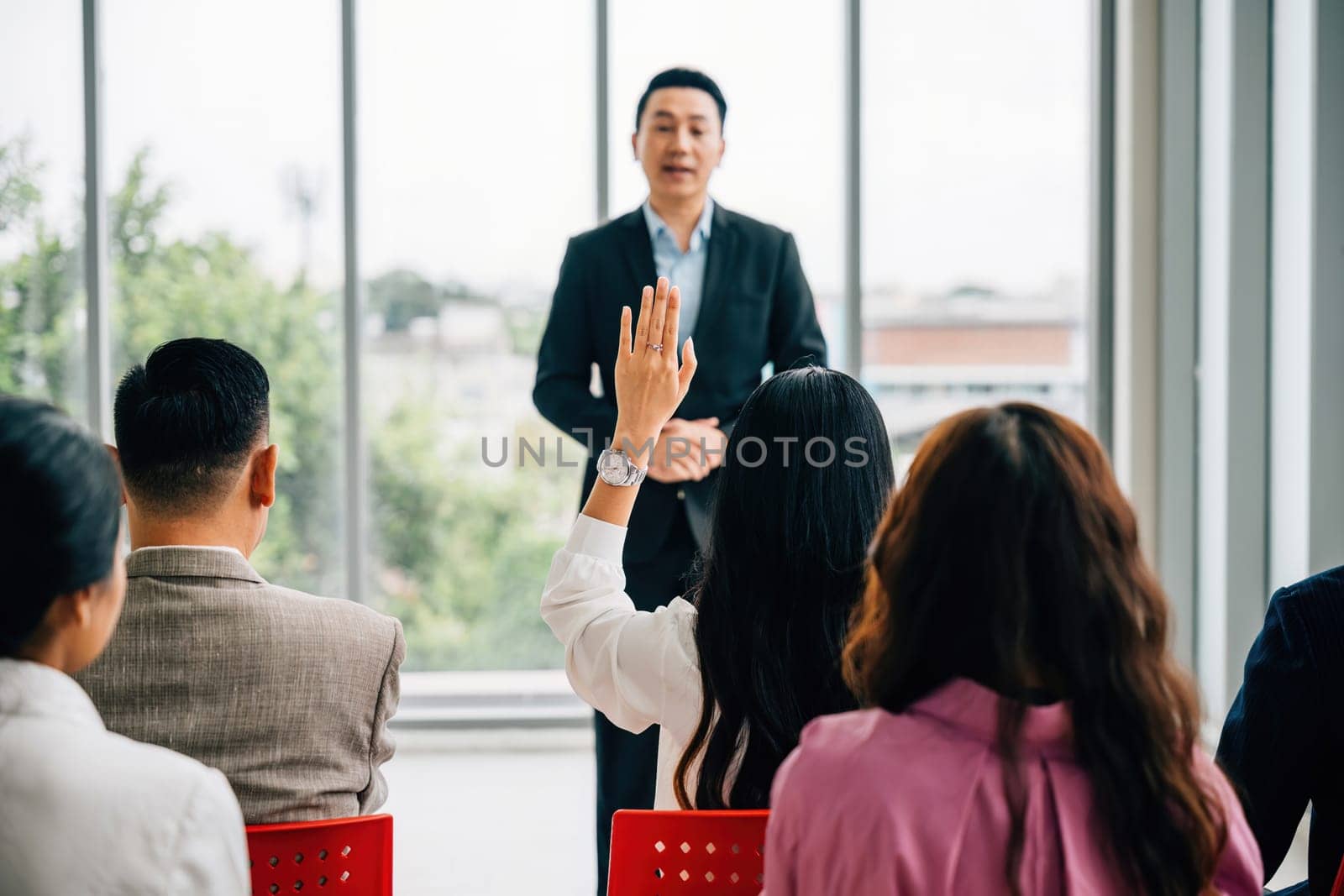 A diverse audience in a conference raises their hands for questions, voting, or volunteering, emphasizing teamwork and audience interaction during this corporate event. by Sorapop