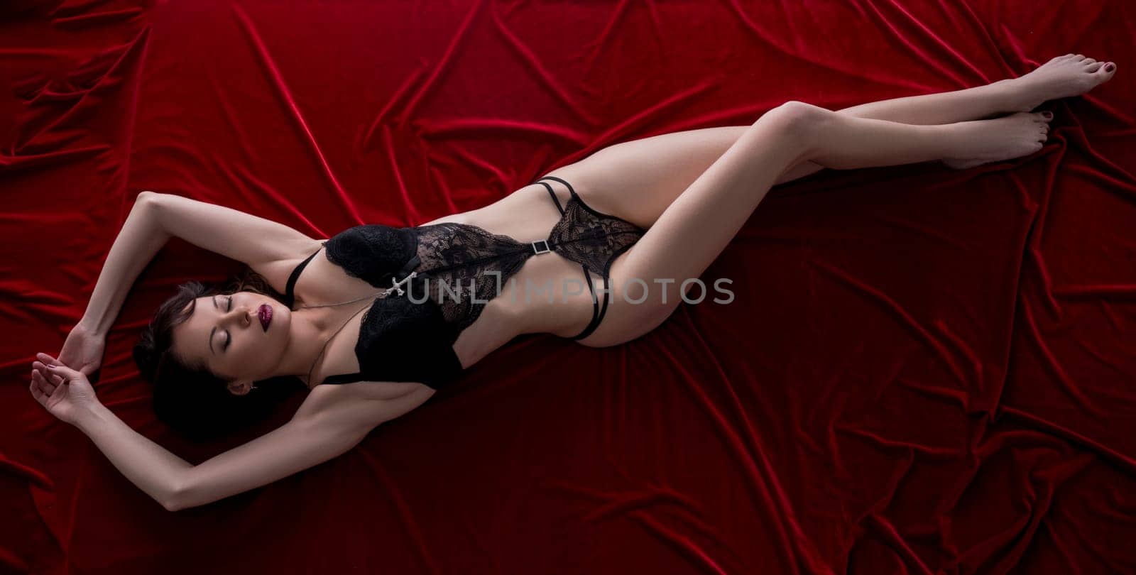 Woman posing in bodysuit lying on velvet bed sheet by rivertime