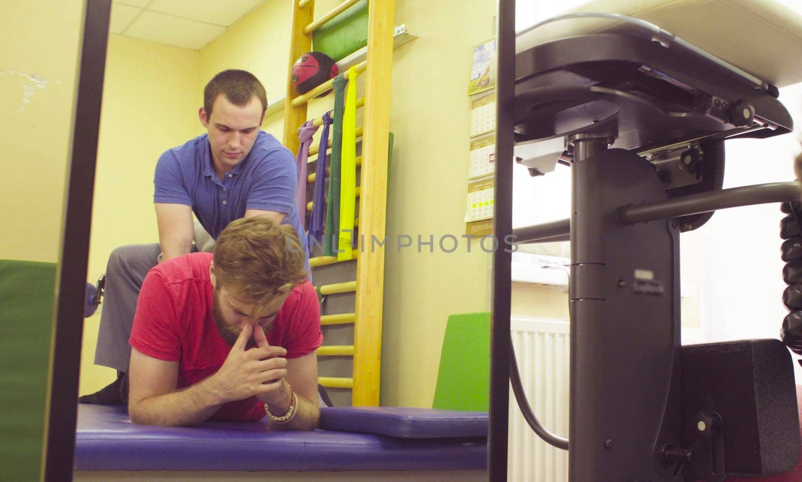 Doctor physical therapist doing massging a back for young disabled man in a rehabilitation clinic.