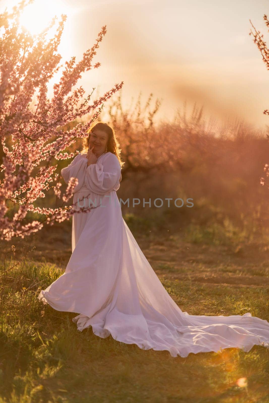 Woman blooming peach orchard. Against the backdrop of a picturesque peach orchard, a woman in a long white dress enjoys a peaceful walk in the park, surrounded by the beauty of nature. by Matiunina