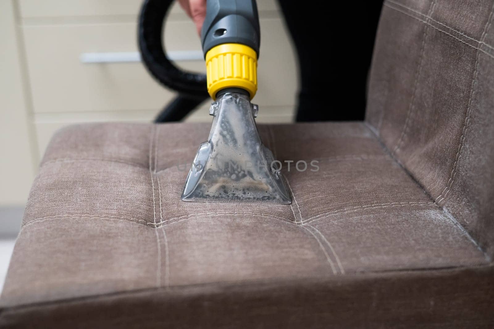 Woman cleaning a fabric chair with a professional washing vacuum cleaner. by mrwed54