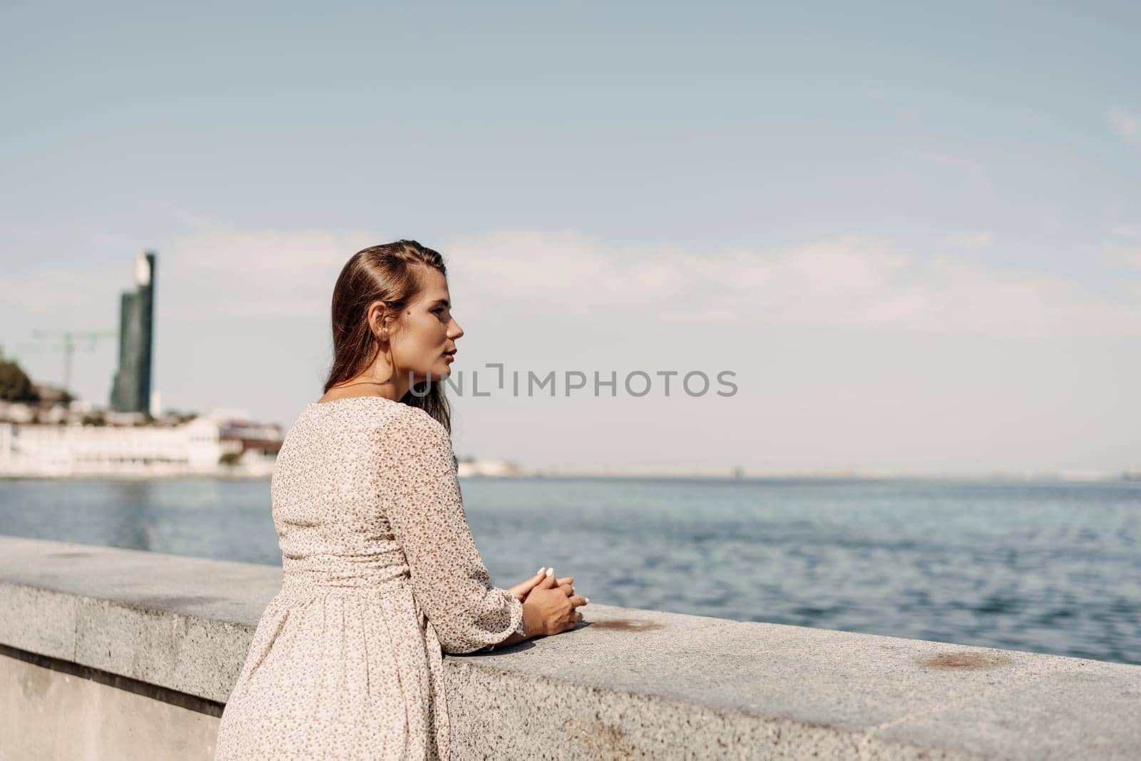 woman stands on a ledge overlooking the ocean. She is wearing a white dress and has her hands on her hips. The scene is peaceful and serene, with the water and sky providing a calming backdrop by Matiunina