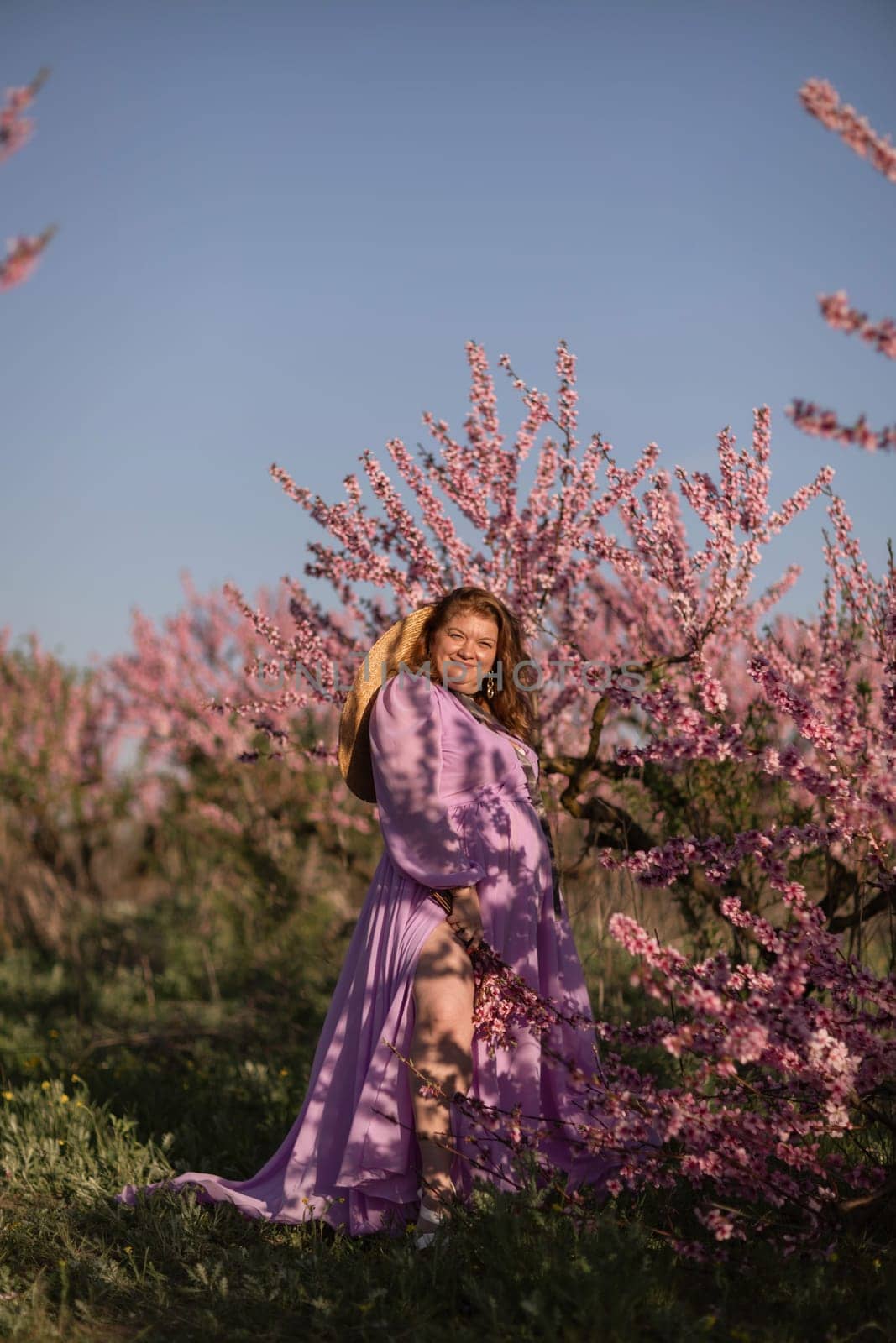 Woman blooming peach orchard. Against the backdrop of a picturesque peach orchard, a woman in a long pink dress and hat enjoys a peaceful walk in the park, surrounded by the beauty of nature. by Matiunina