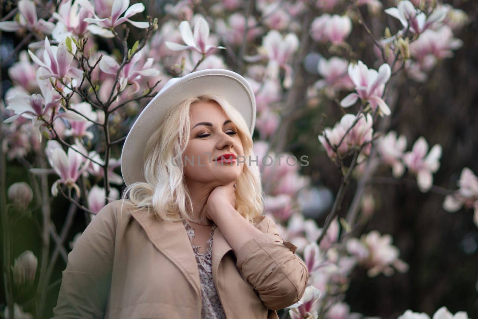 Magnolia flowers woman. A blonde woman wearing a white hat stands in front of a tree full of pink flowers. She is wearing a brown jacket and a necklace. by Matiunina