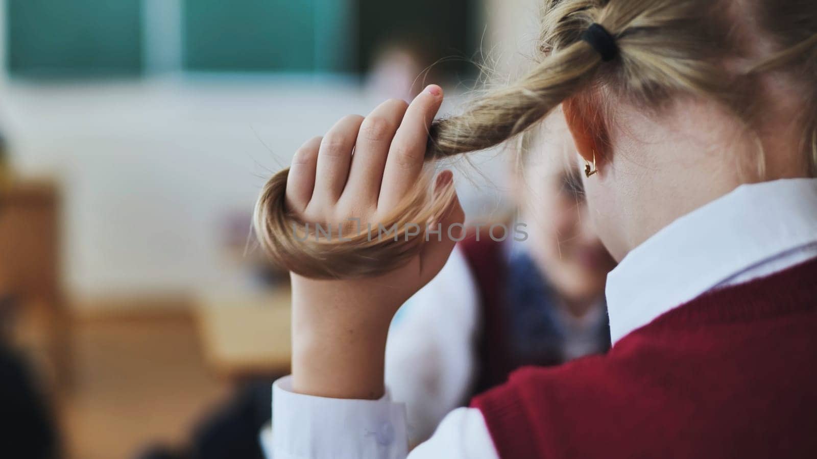 A girl touches a ponytail of her hair during class. by DovidPro