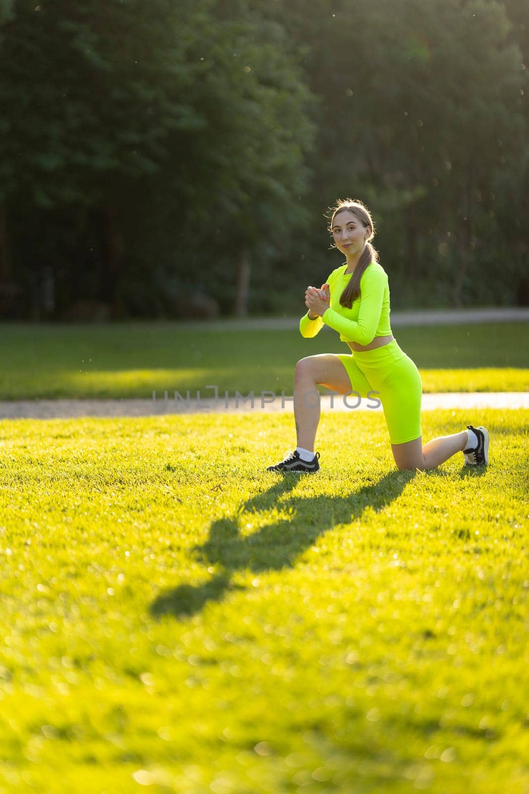 A woman in a neon yellow outfit is doing a yoga pose on a grassy field by Studia72
