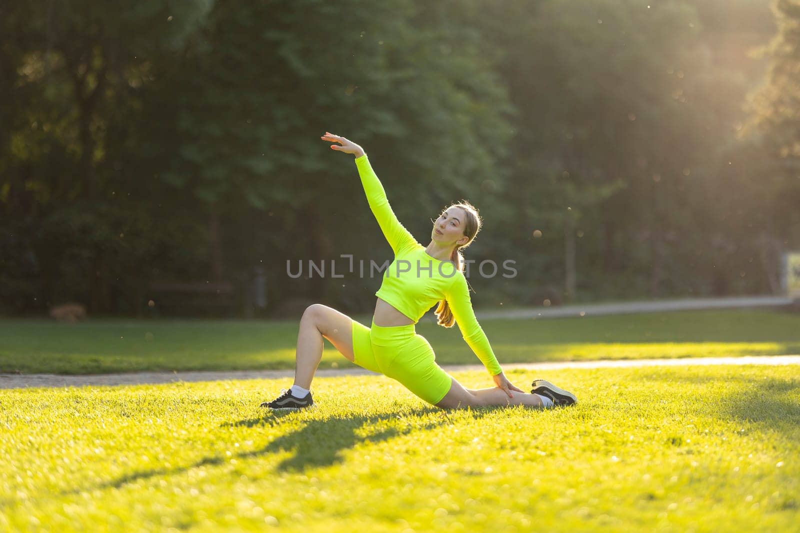 A woman in a neon yellow outfit is doing a yoga pose on a grassy field. The bright colors of her outfit and the lush green grass create a cheerful and energetic mood